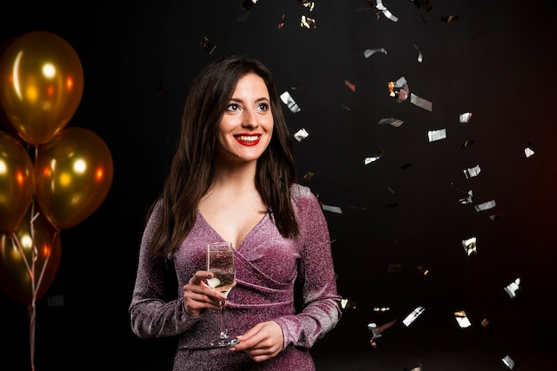 Mujer posando con copa de champán y confeti en la fiesta