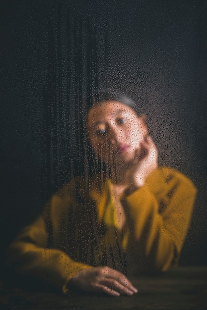 Mujer posando detrás de la ventana con gotas de lluvia en él