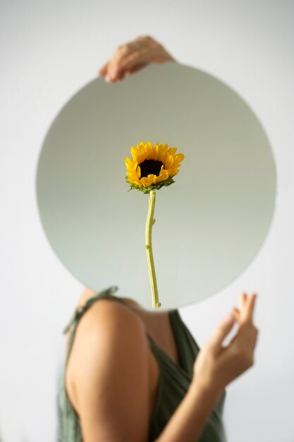 Mujer posando con espejo redondo y flor.