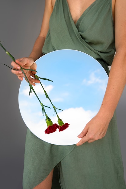 Mujer posando con espejo redondo y flor.