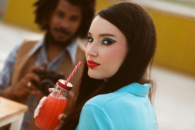 Mujer posando en estilo retro con bebida mientras el hombre toma fotos con cámara