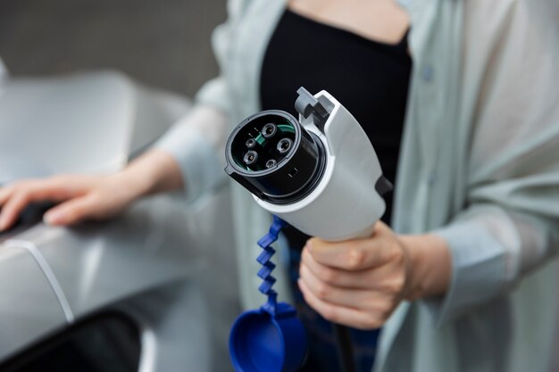 Mujer posando junto al cargador eléctrico y sosteniendo