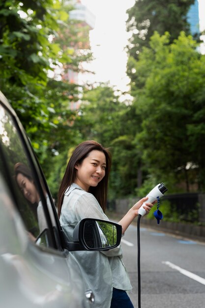 Mujer posando junto al cargador eléctrico y sosteniendo