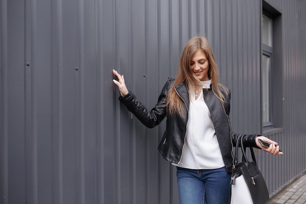 Mujer posando con una mano en una pared y bolsa de la compra en la otra