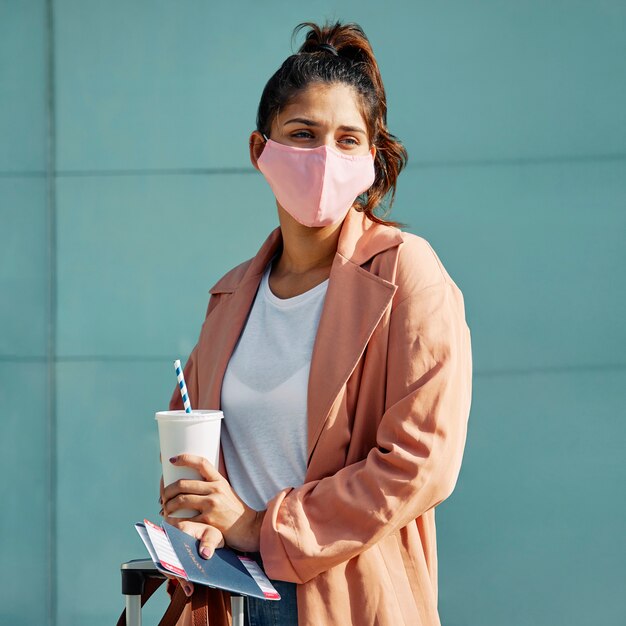 Mujer posando con máscara médica y pasaporte en el aeropuerto durante la pandemia