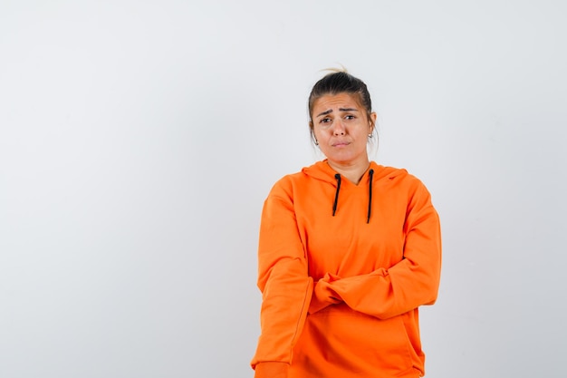 Mujer posando mientras está de pie en una sudadera con capucha naranja y mirando molesto