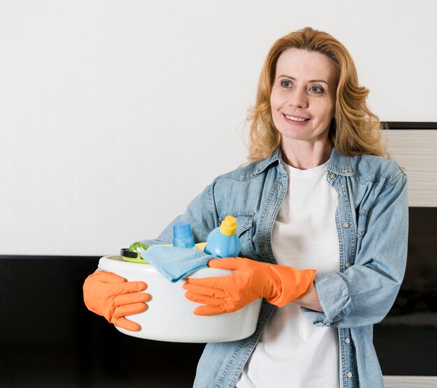 Mujer posando mientras sostiene la cesta de productos de limpieza