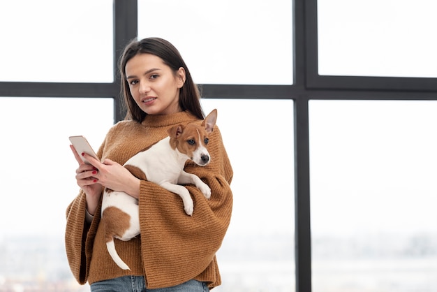 Foto gratuita mujer posando mientras sostiene el perro y el teléfono inteligente