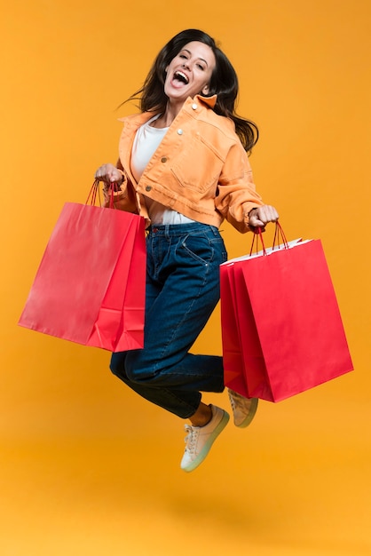 Mujer posando y saltando sosteniendo bolsas de la compra.