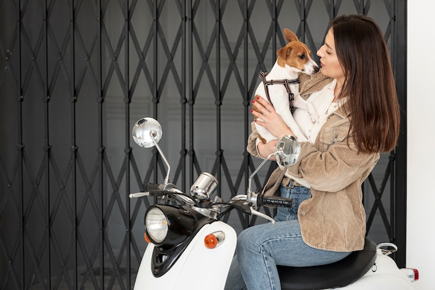 Mujer posando en scooter mientras sostiene a su perro