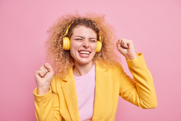 Mujer positiva con cabello rizado natural baila sin preocupaciones hace que triumph dance sonríe disfruta escuchando pistas de audio a través de auriculares inalámbricos