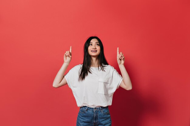 Mujer positiva con camiseta blanca señala con el dedo hacia arriba y sonríe