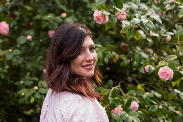 Mujer positiva cerca de flores rosadas que crecen en las ramitas verdes del arbusto