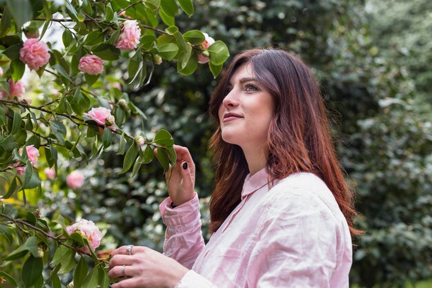 Mujer positiva cerca de flores rosadas que crecen en ramitas verdes