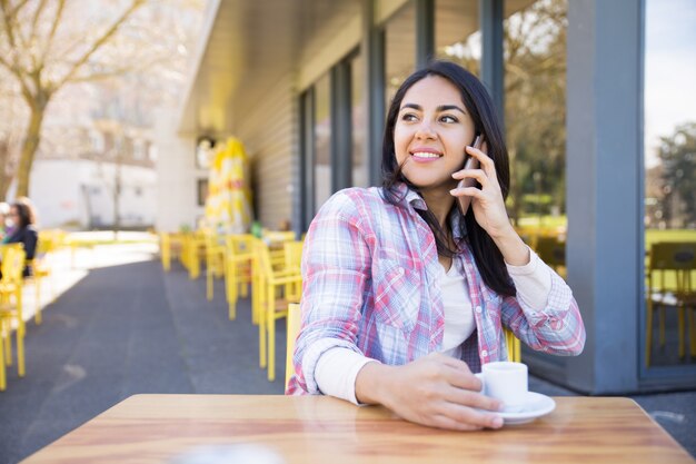 Mujer positiva hablando por teléfono y tomando café