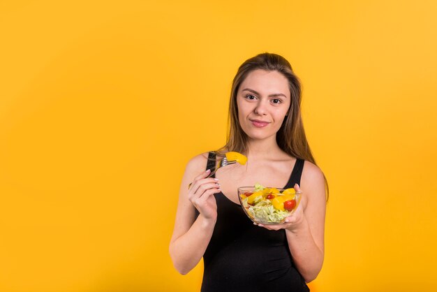 Mujer positiva joven con tenedor y plato de ensalada