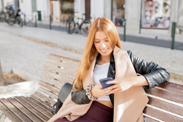 Mujer positiva mensajes de texto sms y sentado en el banco
