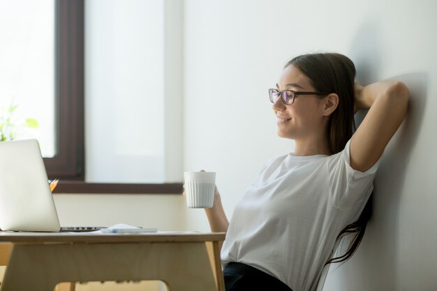 Mujer positiva milenaria relajante en el lugar de trabajo en la oficina