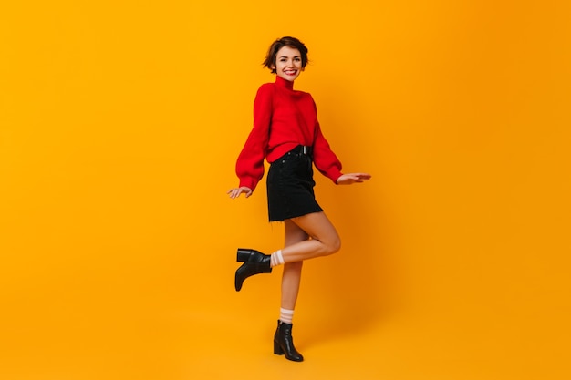 Mujer positiva con pelo corto bailando sobre pared amarilla