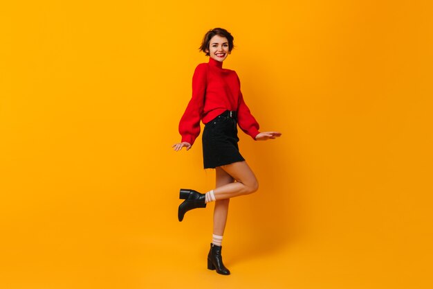 Mujer positiva con pelo corto bailando sobre pared amarilla