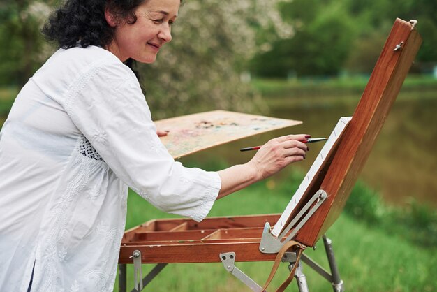 Mujer positiva. Retrato de pintor maduro con cabello rizado negro en el parque al aire libre