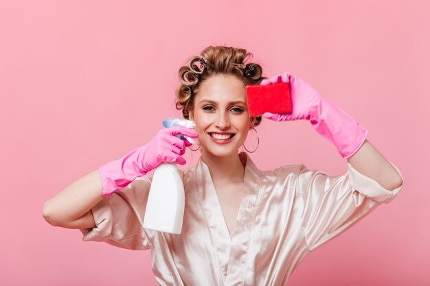 Mujer positiva con rizadores de pelo tiene esponja para lavar platos y limpiador de espejos