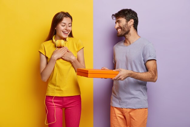 La mujer positiva siente gratitud por recibir un regalo de su novio, expresa buenas emociones. Hombre cariñoso regala caja de cartón con sorpresa a su novia, viene a felicitar con cumpleaños