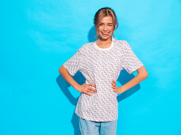 Mujer positiva sonriendo. Modelo divertido posando junto a la pared azul en el estudio. Muestra lengua y guiños