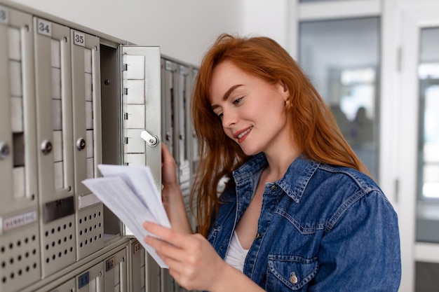 Foto gratuita mujer positivamente vestida de manera casual sosteniendo una nueva carta de la entrega postal sacando su correo de su buzón