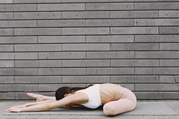 Mujer practicando yoga avanzado contra un muro urbano oscuro