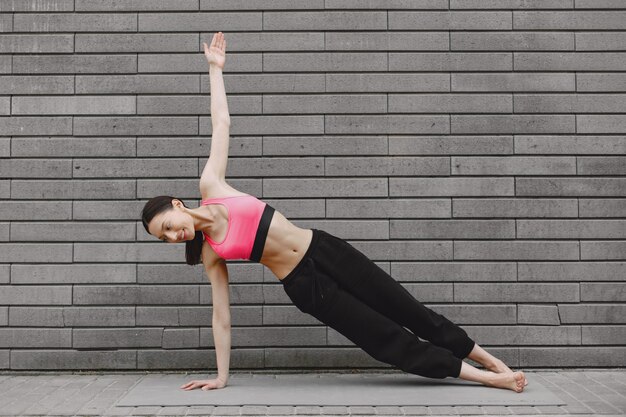 Mujer practicando yoga avanzado contra un muro urbano oscuro