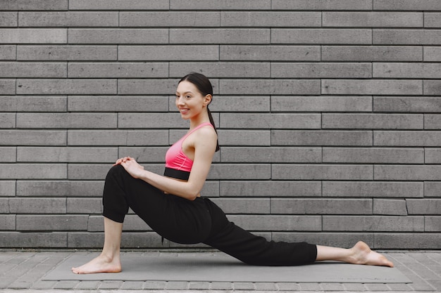 Mujer practicando yoga avanzado contra un muro urbano oscuro