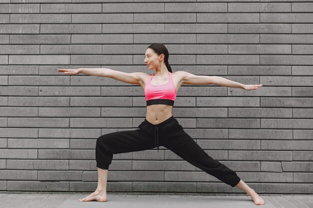 Mujer practicando yoga avanzado contra un muro urbano oscuro