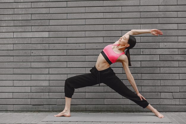 Mujer practicando yoga avanzado contra un muro urbano oscuro