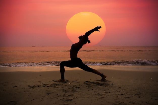 Mujer practicando yoga con el sol detrás de ella