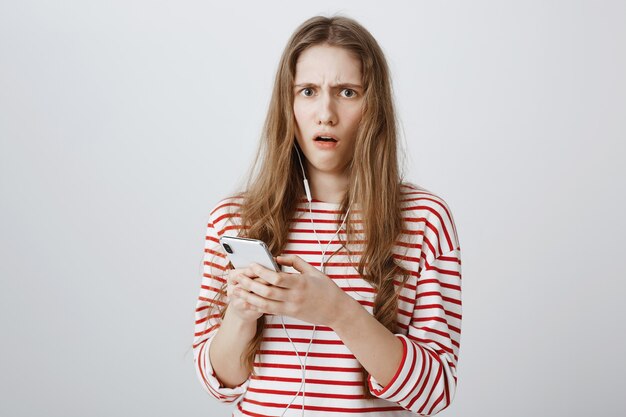 Mujer preocupada y conmocionada mira preocupada después de leer un extraño mensaje en el teléfono móvil
