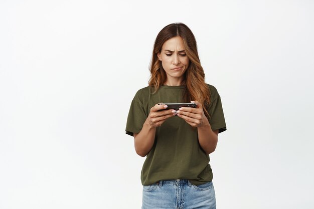 Mujer preocupada frunciendo el ceño, mirando molesto a la pantalla del teléfono inteligente horizontal