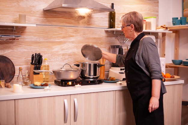 Mujer preparando la comida en la cocina de gas para una cena romántica con su marido. Mujer jubilada cocinando alimentos nutritivos para ella y el hombre para celebrar el aniversario de la relación.