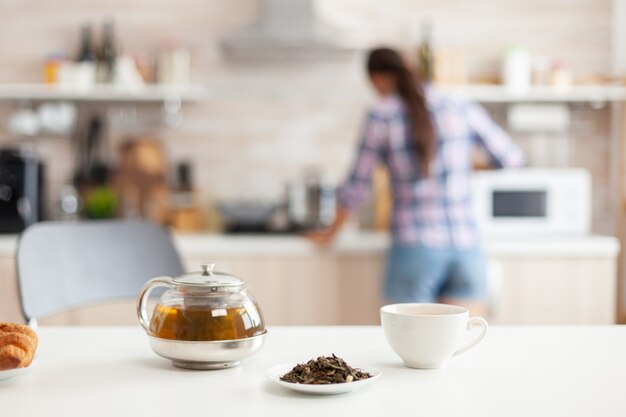 Mujer preparando el desayuno en la cocina y hierbas aromáticas para té caliente