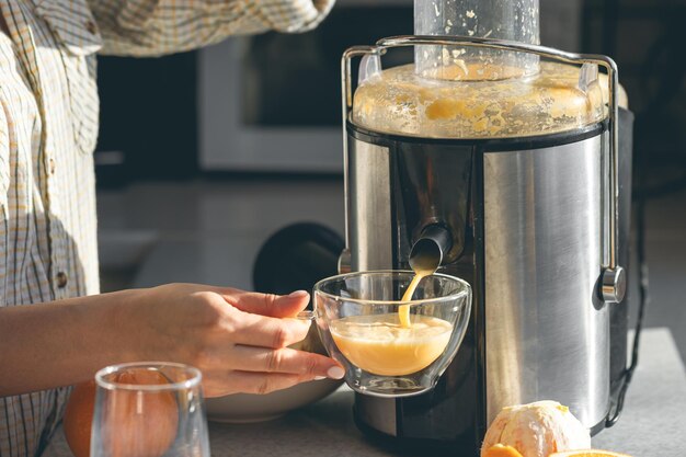 Mujer preparando jugo de naranja fresco para el desayuno en la cocina