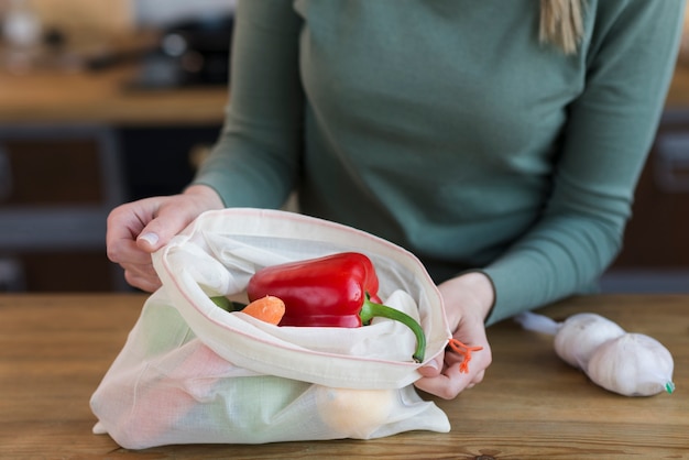 Mujer de primer plano abriendo bolsa reutilizable con verduras