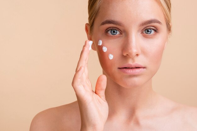 Mujer de primer plano con crema para la cara mirando a la cámara