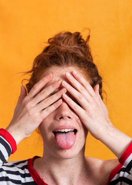 Mujer de primer plano con lengua afuera cubriendo sus ojos