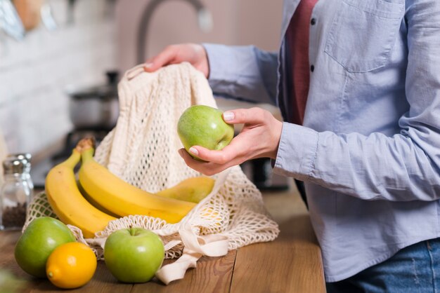 Mujer de primer plano sacando frutas orgánicas de bolsa ecológica