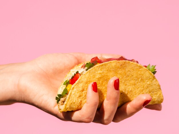 Mujer del primer que sostiene el taco con el fondo rosado