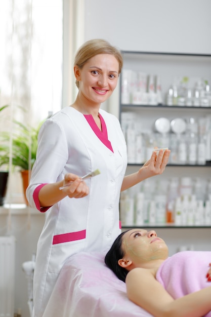 Mujer profesional aplicando una crema verde con un pincel y sonriendo