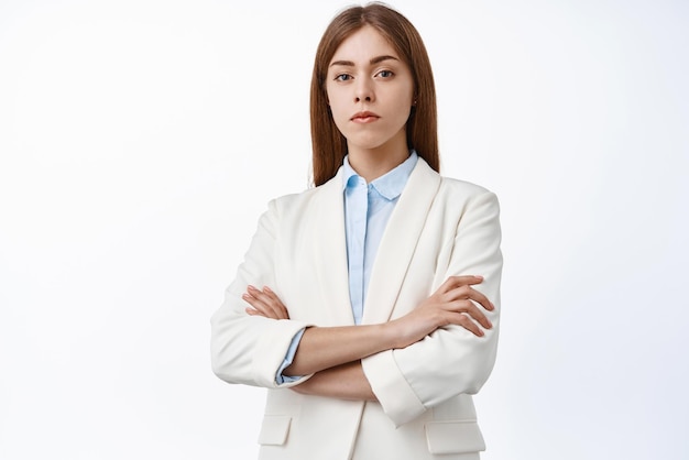 Mujer profesional seria y segura de sí misma en traje de negocios con los brazos cruzados en el pecho, determinada con expresión de cara segura de sí misma, fondo blanco