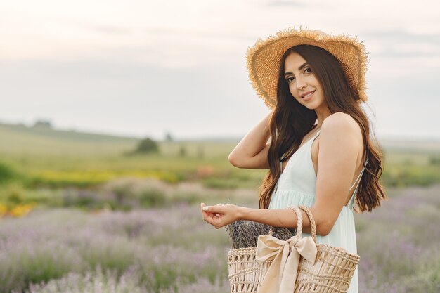 Mujer provenzal relajante en campo de lavanda. Dama con sombrero de paja. Chica con bolso.