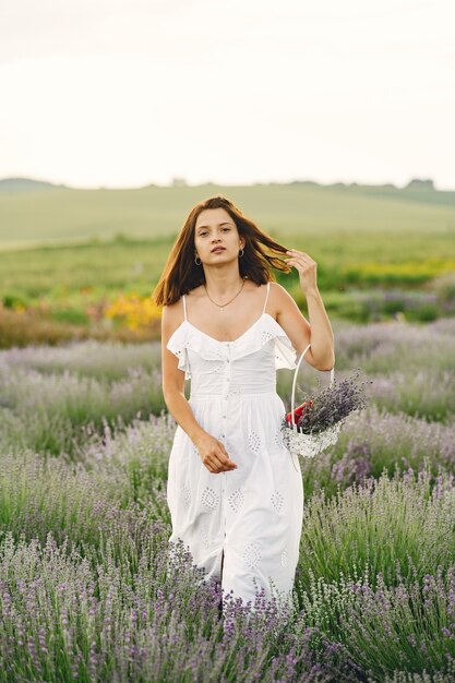 Mujer provenzal relajante en campo de lavanda. Dama con un vestido blanco. Chica con bolso.