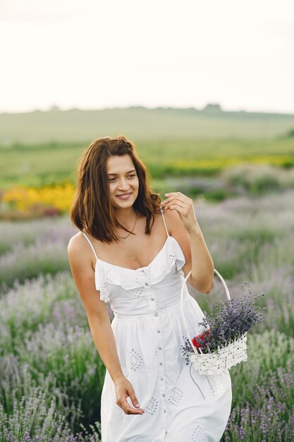 Mujer provenzal relajante en campo de lavanda. Dama con un vestido blanco. Chica con bolso.